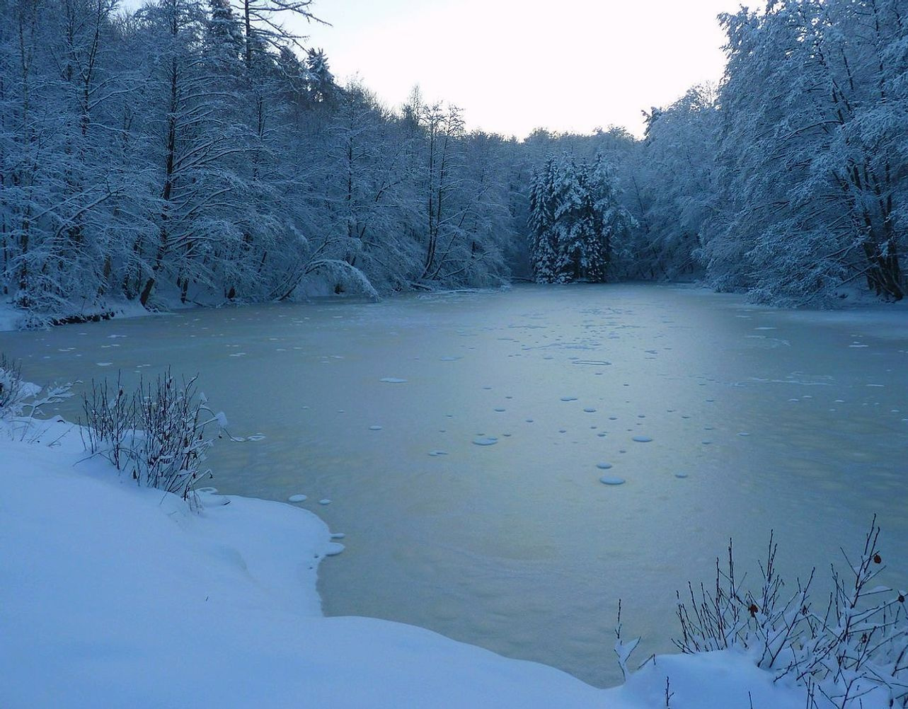 Mesa de madera con mapas del lago de montaña, notas sobre ice safety y cuadernos abiertos